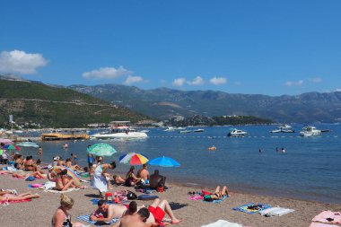 Budva, Karadağ 8.15.22 Çakıl taşı beton plajı Adriyatik denizi Akdeniz. Plaj şemsiyeleri ve havlular. İnsanlar rahatlar, yüzer, güneşlenir. Turizm sektörü. Yaz tatilindeki kadınlar ve erkekler.