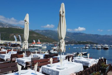 Budva, Karadağ 8.15.22 Adriyatik denizi Akdeniz Rivierası. Turizm sektörü. Yatlar, tekneler ve eğlence tekneleri. Deniz kenarındaki restoran, ilk sıra. Masalar, sandalyeler, güneş şemsiyeleri ve beyaz masa örtüleri.