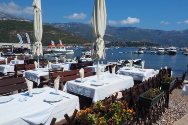 Budva, Karadağ 8.15.22 Adriyatik denizi Akdeniz Rivierası. Turizm sektörü. Yatlar, tekneler ve eğlence tekneleri. Deniz kenarındaki restoran, ilk sıra. Masalar, sandalyeler, güneş şemsiyeleri ve beyaz masa örtüleri.