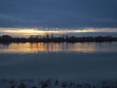 Tranquil scenery sunset Sava river Sremska Macvanska Mitrovica, Serbia. Perfect reflection of trees and afterglow  backlight. Ripples on the water. Horizon. Blue water. Yellow-pink sunset. December. clipart