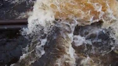 Nehirde akan su. Nehirde su akıyor. Nehir metal borulardan akar. Sarı-beyaz köpük. Karelia, Lososinka Nehri baharda. Seller, tsunami ve iklim değişikliği. Yavaş çekim.