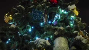 Yılbaşı süslemeleri sokak Noel ağacında. Bir kar tanesi, çelenkler, toplar ve ampuller rüzgarda sallanıyor. Tatil dekoru. Noel ağacı dalında ev yapımı oyuncaklar. Parlayan ve ışıl ışıl çelenkler.