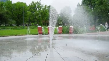 Varşova, Polonya, Park Pieciu Siostr, Warszawa, 04.09.24: Fontanna Ochocka Patelnia. Zahodnij Parkı. Beklenmedik çok yönlü su sıçramaları olan bir çeşme. Bahar günü. Yoldan geçenler geçiyor.
