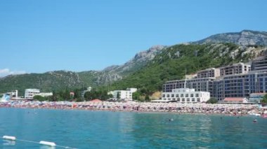 Canj Montenegro 07.21.24 Tatilciler, güneşlenenler ve yüzücülerle dolu bir tekne turu. Oteller, güneş şemsiyeleri, Adriyatik dalgaları, şamandıralar. Plaj turizmi. Tatil seyahati. Yaz günü. Kumlu çakıl taşı plajı.