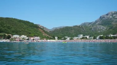 Canj Montenegro 07.21.24 Tatilciler, güneşlenenler ve yüzücülerle dolu bir tekne turu. Oteller, güneş şemsiyeleri, Adriyatik dalgaları, şamandıralar. Plaj turizmi. Tatil seyahati. Yaz günü. Kumlu çakıl taşı plajı