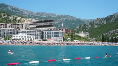 Canj Montenegro 07.21.24 Tatilciler, güneşlenenler ve yüzücülerle dolu bir tekne turu. Oteller, güneş şemsiyeleri, Adriyatik dalgaları, şamandıralar. Plaj turizmi. Tatil seyahati. Yaz günü. Kumlu çakıl taşı plajı.