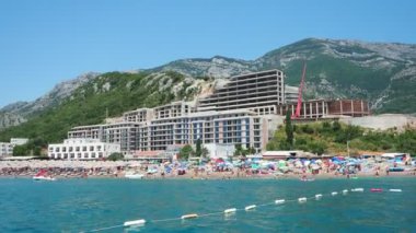 Canj Montenegro 07.21.24 Tatilciler, güneşlenenler ve yüzücülerle dolu bir tekne turu. Oteller, güneş şemsiyeleri, Adriyatik dalgaları, şamandıralar. Plaj turizmi. Tatil seyahati. Yaz günü. Kumlu çakıl taşı plajı.
