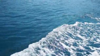 Yat dalgaları gök mavisi Adriyatik Akdeniz 'inde hareket ediyor. Mavi su yüzeyi, köpük kabarcıkları. Seyahat, tekne gezileri, yaz tatilleri, Karadağ, Budva bölgesi, mağaralar körfezi, Petrovac yakınlarındaki köpekbalığı koyları..