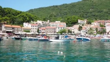 Petrovac, Karadağ 07.22.24 Tatilciler, güneşlenenler ve yüzücülerle kıyıdan geçen bir tekne. Oteller, güneş şemsiyeleri, Adriyatik dalgaları, şamandıralar. Plaj turizmi. Tatil seyahati. Yaz günü. Kumlu çakıl.