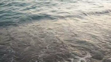 Dalgalar sersemletici günbatımında yavaşça kıyıya vurur. Altın güneş ışığı, dalgaların kıyıya vuruşunu yansıtır. Gün batımında deniz kenarında sakin bir atmosfer yaratır. Karadağ yazı, Canj.