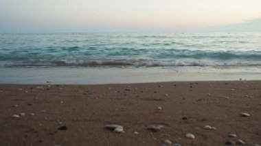 Dalgalar sersemletici günbatımında yavaşça kıyıya vurur. Altın güneş ışığı, dalgaların kıyıya vuruşunu yansıtır. Gün batımında deniz kenarında sakin bir atmosfer yaratır. Karadağ yazı, Canj.