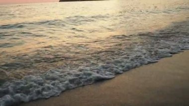 Dalgalar sersemletici günbatımında yavaşça kıyıya vurur. Altın güneş ışığı, dalgaların kıyıya vuruşunu yansıtır. Gün batımında deniz kenarında sakin bir atmosfer yaratır. Karadağ yazı, Canj