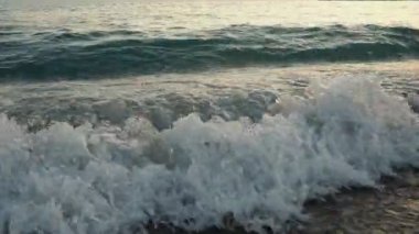 Dalgalar sersemletici günbatımında yavaşça kıyıya vurur. Altın güneş ışığı, dalgaların kıyıya vuruşunu yansıtır. Gün batımında deniz kenarında sakin bir atmosfer yaratır. Karadağ yazı, Canj