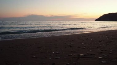 Dalgalar sersemletici günbatımında yavaşça kıyıya vurur. Altın güneş ışığı, dalgaların kıyıya vuruşunu yansıtır. Gün batımında deniz kenarında sakin bir atmosfer yaratır. Karadağ yazı, Canj