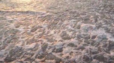 Dalgalar sersemletici günbatımında yavaşça kıyıya vurur. Altın güneş ışığı, dalgaların kıyıya vuruşunu yansıtır. Gün batımında deniz kenarında sakin bir atmosfer yaratır. Karadağ yazı, Canj