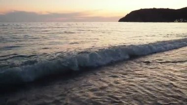 Dalgalar sersemletici günbatımında yavaşça kıyıya vurur. Altın güneş ışığı, dalgaların kıyıya vuruşunu yansıtır. Gün batımında deniz kenarında sakin bir atmosfer yaratır. Karadağ yazı, Canj