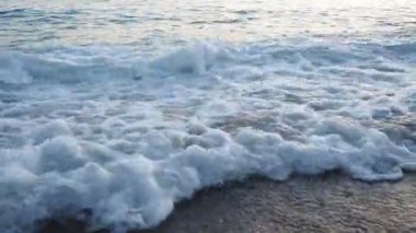 Dalgalar sersemletici günbatımında yavaşça kıyıya vurur. Altın güneş ışığı, dalgaların kıyıya vuruşunu yansıtır. Gün batımında deniz kenarında sakin bir atmosfer yaratır. Karadağ yazı, Canj.