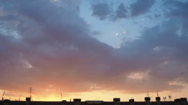 Sarı turuncu günbatımı gökyüzü bulutları. Yumuşak, ılık sarı renkler huzurlu ve huzurlu bir atmosfer yaratıyor. Batan güneşin hafif ışınları altın dokunuşuyla ufku boyuyor. Şehrin çatısında gün batımı. Gerçek zamanlı.