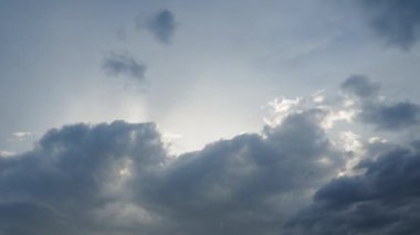 Güneş kalın bulut tabakalarının arasından parlayarak ışık huzmeleri oluşturur. Bulutlar gri, mavi ve beyaz karışımıdır ve bazı bölgeler diğerlerinden daha koyu görünür. Zaman aşımı. Bulutlu Gökyüzü Güneş Işıklarıyla.
