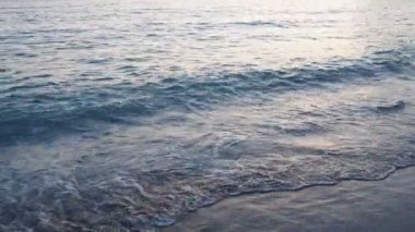 Dalgalar sersemletici günbatımında yavaşça kıyıya vurur. Altın güneş ışığı, dalgaların kıyıya vuruşunu yansıtır. Gün batımında deniz kenarında sakin bir atmosfer yaratır. Karadağ yazı, Canj.