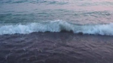 Dalgalar sersemletici günbatımında yavaşça kıyıya vurur. Pembe güneş ışığı dalgalardan yansıyarak kıyıya vurur ve gün batımında deniz kenarında sakin bir atmosfer yaratır. Karadağ yazı. Pembe mavi renk