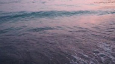 Dalgalar sersemletici günbatımında yavaşça kıyıya vurur. Pembe güneş ışığı dalgalardan yansıyarak kıyıya vurur ve gün batımında deniz kenarında sakin bir atmosfer yaratır. Karadağ yazı. Pembe mavi renk