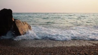 Dalgalar günbatımında okyanusta yavaşça kayalık kıyılarda tur atar. Altın güneş ışığı, dalgaların kıyıya vuruşunu yansıtır. Gün batımında deniz kenarında sakin bir atmosfer yaratır. Karadağ yazı, Canj.