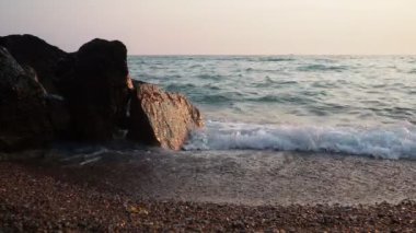 Dalgalar günbatımında okyanusta yavaşça kayalık kıyılarda tur atar. Altın güneş ışığı, dalgaların kıyıya vuruşunu yansıtır. Gün batımında deniz kenarında sakin bir atmosfer yaratır. Karadağ yazı, Canj.