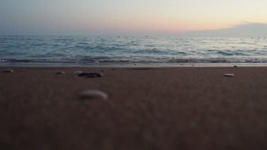 Dalgalar sersemletici günbatımında yavaşça kıyıya vurur. Pembe güneş ışığı dalgaları yansıtır ve kumlu sahile yuvarlanır. Gün batımında deniz yoluyla sakin bir atmosfer yaratır. Karadağ yazı. Mavi saat.