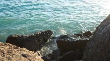 Dalgalar günbatımında okyanusta yavaşça kayalık kıyılarda tur atar. Altın güneş ışığı, dalgaların kıyıya vuruşunu yansıtır. Gün batımında deniz kenarında sakin bir atmosfer yaratır. Karadağ yazı, Canj
