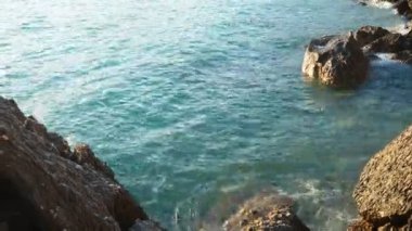 Dalgalar günbatımında okyanusta yavaşça kayalık kıyılarda tur atar. Altın güneş ışığı, dalgaların kıyıya vuruşunu yansıtır. Gün batımında deniz kenarında sakin bir atmosfer yaratır. Karadağ yazı, Canj.