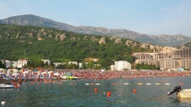 Canj, Karadağ 07.20.2024 Boat ve tatilciler, güneşlenenler ve yüzücülerle dolu bir sahil. Oteller, güneş şemsiyeleri, Adriyatik dalgaları, şamandıralar. Plaj turizmi. Tatil seyahati. Yaz günü. Çakıl taşı plajı.