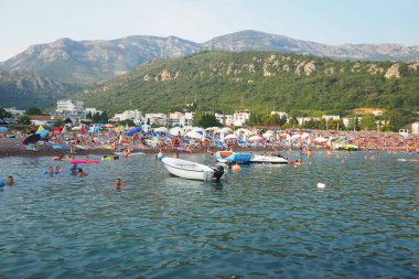 Canj, Karadağ 07.20.2024 Boat ve tatilciler, güneşlenenler ve yüzücülerle dolu bir sahil. Oteller, güneş şemsiyeleri, Adriyatik dalgaları, şamandıralar. Plaj turizmi. Tatil seyahati. Yaz günü. Çakıl taşı plajı.