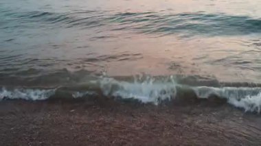 Dalgalar sersemletici günbatımında yavaşça kıyıya vurur. Altın güneş ışığı, dalgaların kıyıya vuruşunu yansıtır. Gün batımında deniz kenarında sakin bir atmosfer yaratır. Karadağ yazı, Canj.