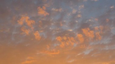 Güzel resimli günbatımı. Batan güneş küçük bulutları parlak turuncu ve sarıya boyar. Arka plan olarak mavi gökyüzü. Hafif bulutlar gökyüzünü kaplıyor ve havanın değişeceğine söz veriyor..