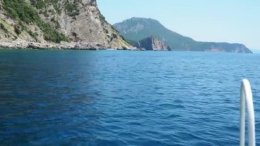 Durgun sular, berrak mavi gökyüzünün altında sonsuza dek uzanıyor. Tekne ön planındaki gösteriler ayrıntıları yıpratırken, uzak tepeler sakin bir zemin oluşturuyor. RT Dubovica Kraljicina Plaza ve Canj, Karadağ yakınlarındaki Kayalıkları