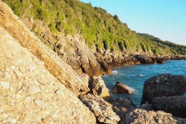 Güneş ufukta batarken dalgalar yavaşça engebeli kayalara çarpıyor. Doğal harikalarla dolu bu kıyı bölgesinin huzurlu güzelliğini tecrübe edin. Canj, Karadağ, Adriyatik denizi.