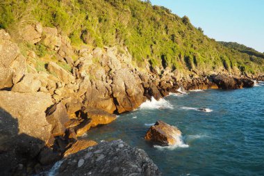 Güneş ufukta batarken dalgalar yavaşça engebeli kayalara çarpıyor. Doğal harikalarla dolu bu kıyı bölgesinin huzurlu güzelliğini tecrübe edin. Canj, Karadağ, Adriyatik denizi.