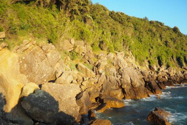 Güneş ufukta batarken dalgalar yavaşça engebeli kayalara çarpıyor. Doğal harikalarla dolu bu kıyı bölgesinin huzurlu güzelliğini tecrübe edin. Canj, Karadağ, Adriyatik denizi.