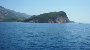 Uzak bir sahil şeridi boyunca berrak mavi suların üzerinde yükselen görkemli uçurumlar. Resimli manzara barışçıl ortamda doğa güzelliğini sergiliyor. RT Dubovica Buljarica, Svetac Rock, Karadağ yakınlarındaki Kayalıkları