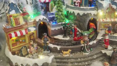 Büyüleyici bir Noel köyü renkli heykelciklerle, karla kaplı evlerin arasında dolanan bir trenle ve şenlikli dekorasyonlarla canlanıyor ve büyülü bir tatil atmosferi yaratıyor. Oyuncak komik kurulum.