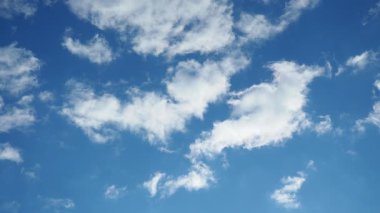 Yumuşak, beyaz bulutlar parlak mavi bir alanda tembelce süzülür ve sakin bir atmosfer yaratır. Güneş ışıl ışıl parlıyor, bulutlar sürüklenirken gölgeler yavaş yavaş kayıyor. Gerçek zamanlı, ağır çekim gökyüzü