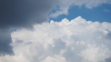 Büyüleyici bir manzara, parlak mavi gökyüzünde zarif bir şekilde süzülen tüylü, beyaz bulutları ortaya çıkarır. Kara bulutların gölgeleri büyüleyici bir zıtlık yaratır, dinamik ve dinamik bir atmosfer yaratır..