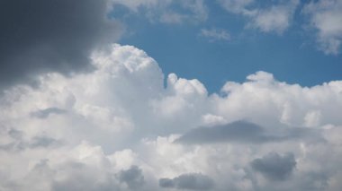 Büyüleyici bir manzara, parlak mavi gökyüzünde zarif bir şekilde süzülen tüylü, beyaz bulutları ortaya çıkarır. Kara bulutların gölgeleri büyüleyici bir zıtlık yaratır, dinamik ve dinamik bir atmosferi çağrıştırır. Gerçek zamanlı..