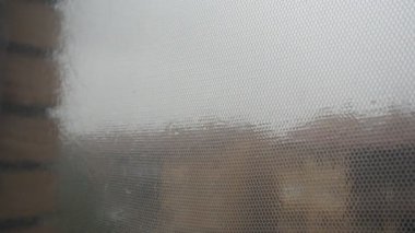 Şiddetli yağmurda pencereden bak. Damlalar bardağı ve cibinliği ıslatıyor. Hava kötüleşiyor. Yağmur damlaları zarif bir şekilde pencereden kayarak kasvetli bir şehir manzarasını gözler önüne seriyor.