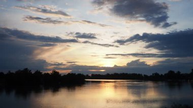 Altın güneş, gece çökerken su yüzeyinde dans eder. Bereketli ağaçlar, doğal güzelliklere rahatlama ve tefekküre davetiye çıkaran sakin bir zemin oluşturuyorlar. River Sava, Sırbistan, Srem.