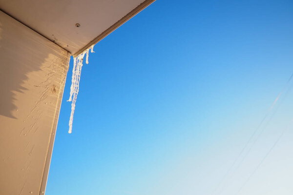 Long icicles dangle from the edge of a roof, capturing sunlight and glistening against a clear blue sky. This winter scene evokes a sense of tranquility and the beauty of cold weather.