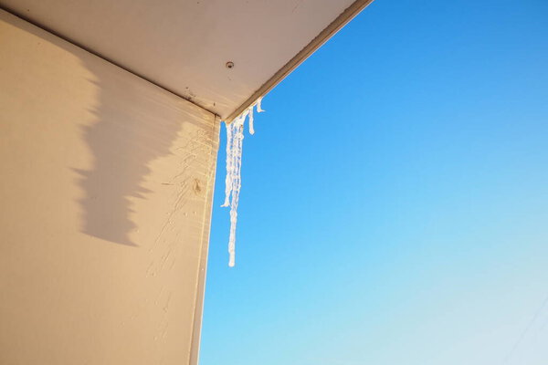 Long icicles dangle from the edge of a roof, capturing sunlight and glistening against a clear blue sky. This winter scene evokes a sense of tranquility and the beauty of cold weather