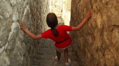 Karadağ 'ın Stari Bar kentindeki eski taş merdivenlerde küçük bir kız geziniyor. Tarihe ait bir hikaye anlatan kırsal duvarlarla çevrili bir şekilde aşağıya iniyor. Antik Akdeniz mimarisi.