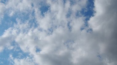 Yumuşak, tüylü bulutlar parlak mavi bir gökyüzünde yavaşça hareket eder. Barışçıl atmosfer, açık havanın güzelliğini ve değişen hava düzenini yakalar..